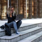 A woman working remotely on laptop outdoors, wearing casual attire in urban Leiden.