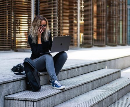 A woman working remotely on laptop outdoors, wearing casual attire in urban Leiden.