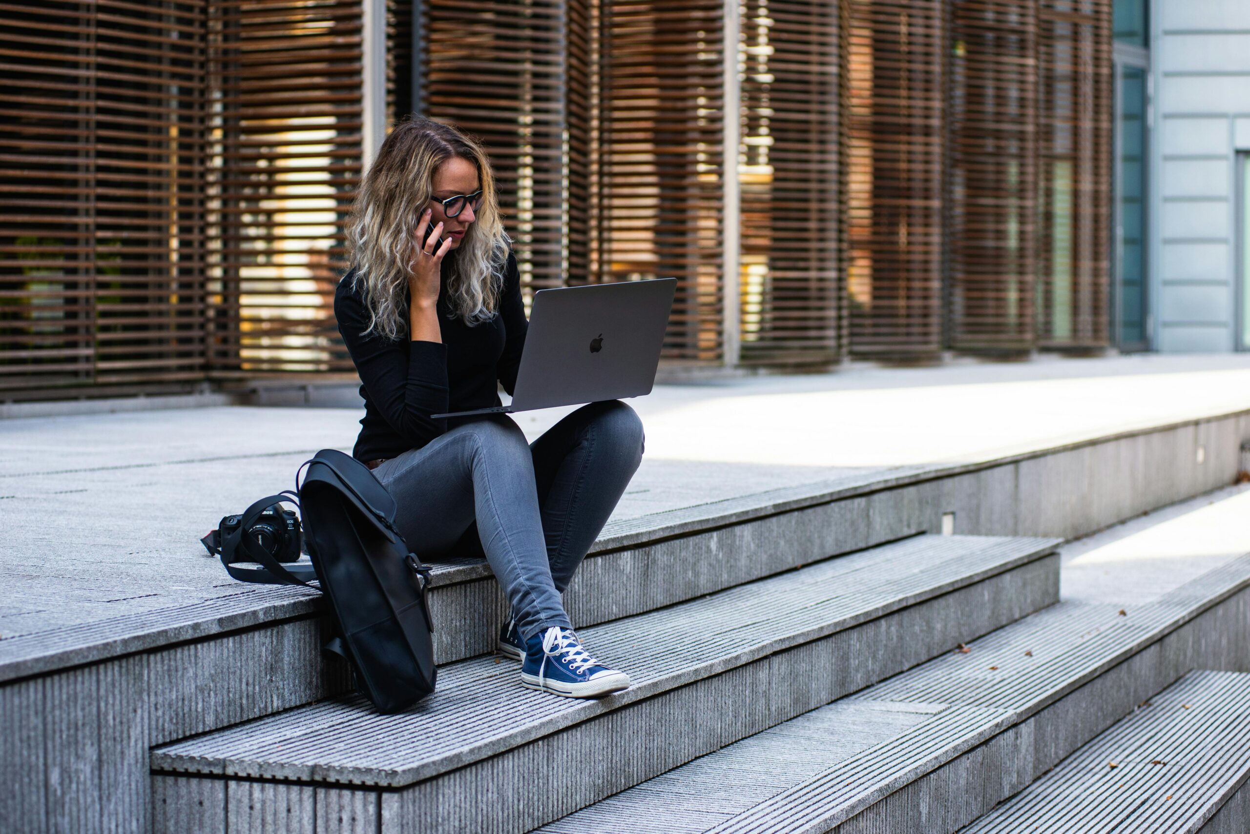 A woman working remotely on laptop outdoors, wearing casual attire in urban Leiden.