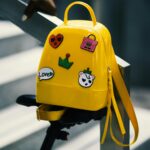 Stylish yellow backpack with playful stickers on a bicycle saddle outdoors.