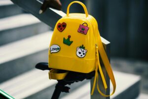 Stylish yellow backpack with playful stickers on a bicycle saddle outdoors.