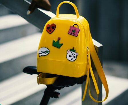 Stylish yellow backpack with playful stickers on a bicycle saddle outdoors.